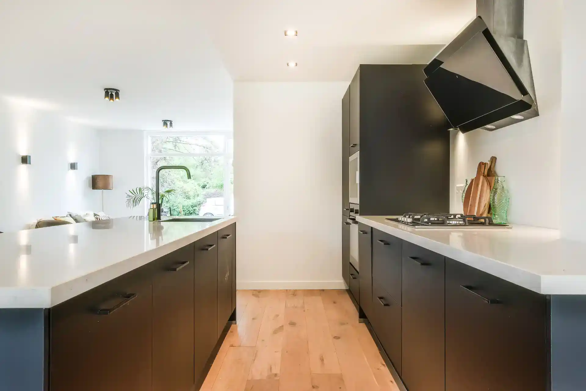 Billedet viser et stilrent køkken med sorte skabe, hvid bordplade og masser af naturligt lys.