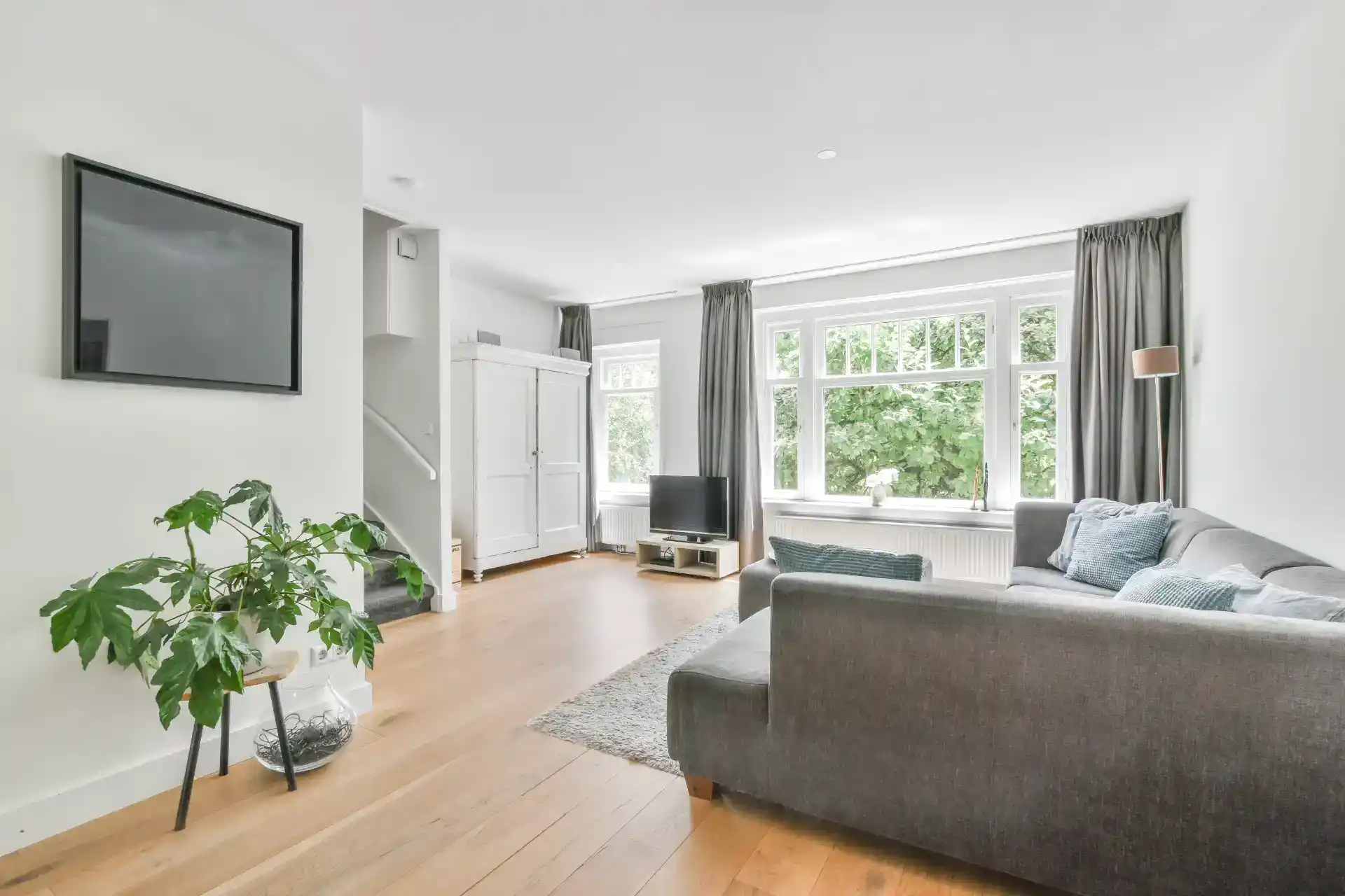 Billedet viser en lys, moderne stue med store vinduer, komfortabel sofa og elegant indretning.