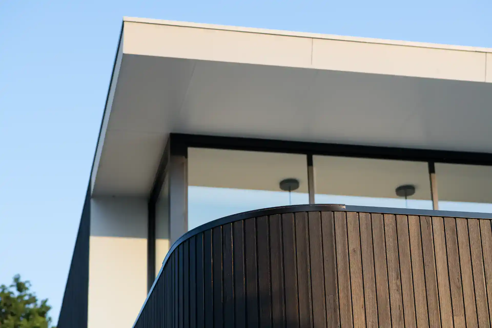 Billedet viser en moderne træbeklædt balkon med glasvæg, del af et arkitektonisk flot byggeri.