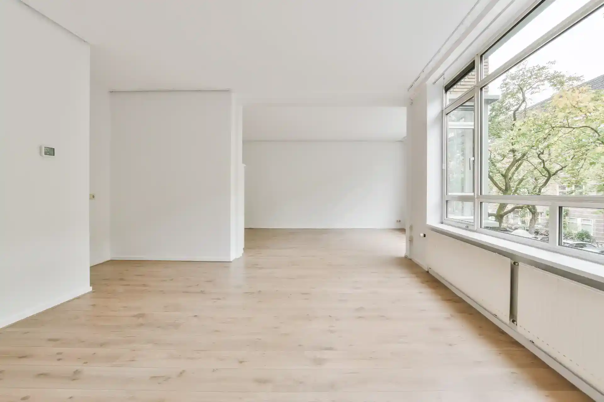 Billedet viser en lys, renoveret lejlighed med store vinduer og trægulv.