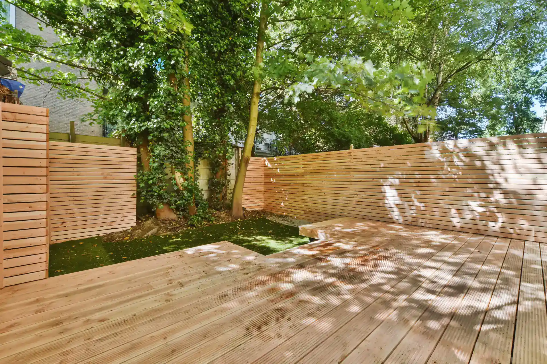 Moderne træterrasse, ideel til udendørs ophold under trækroner, med nyt hegn for privatliv.